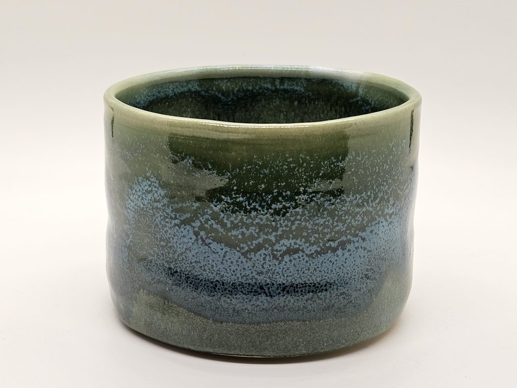 Hand thrown cup glazed with a blue wave over a green base. Made at Moshier Community Art Center. 